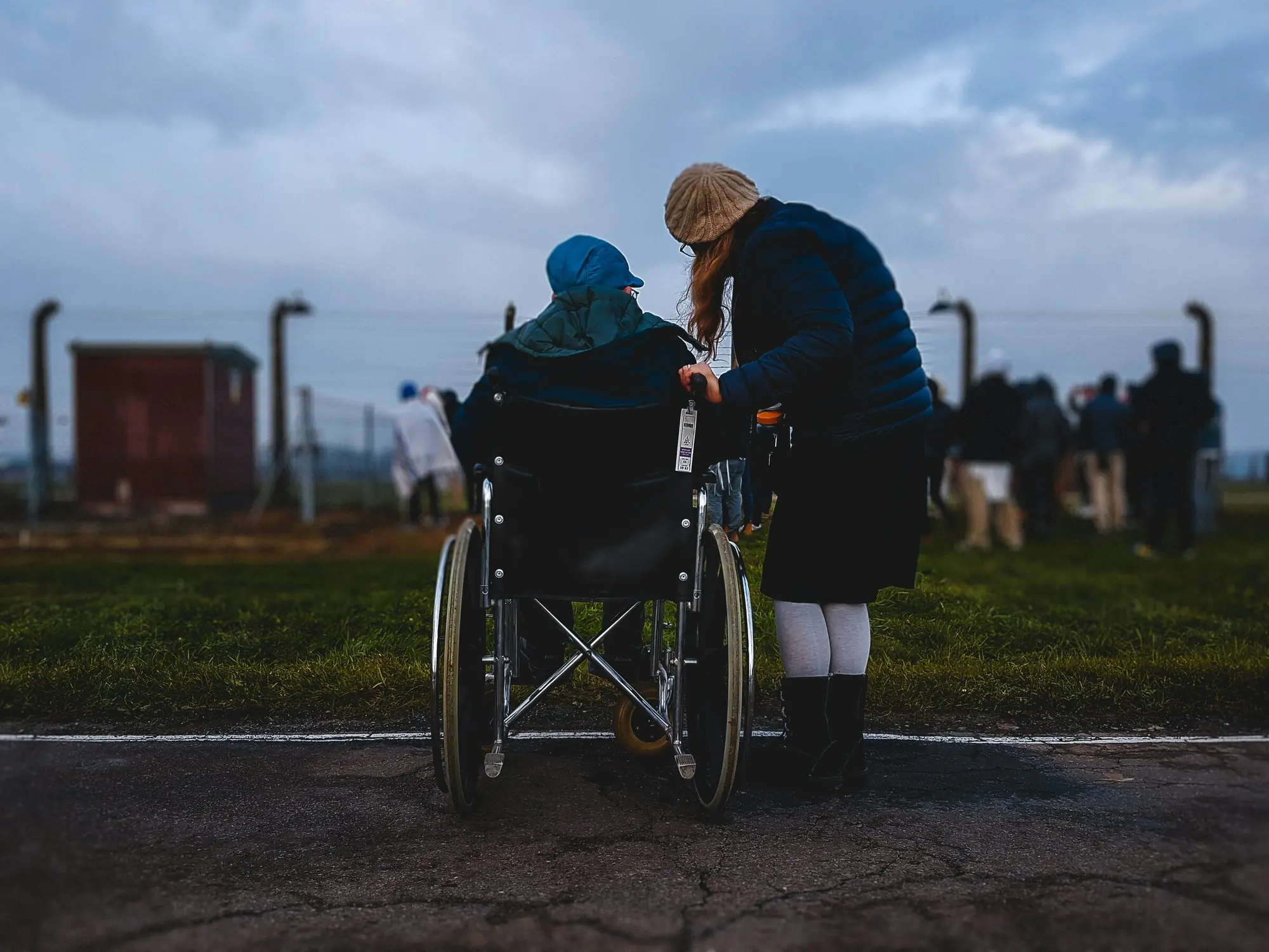 A support worker leans in to talk with a person in a wheelchair outdoors