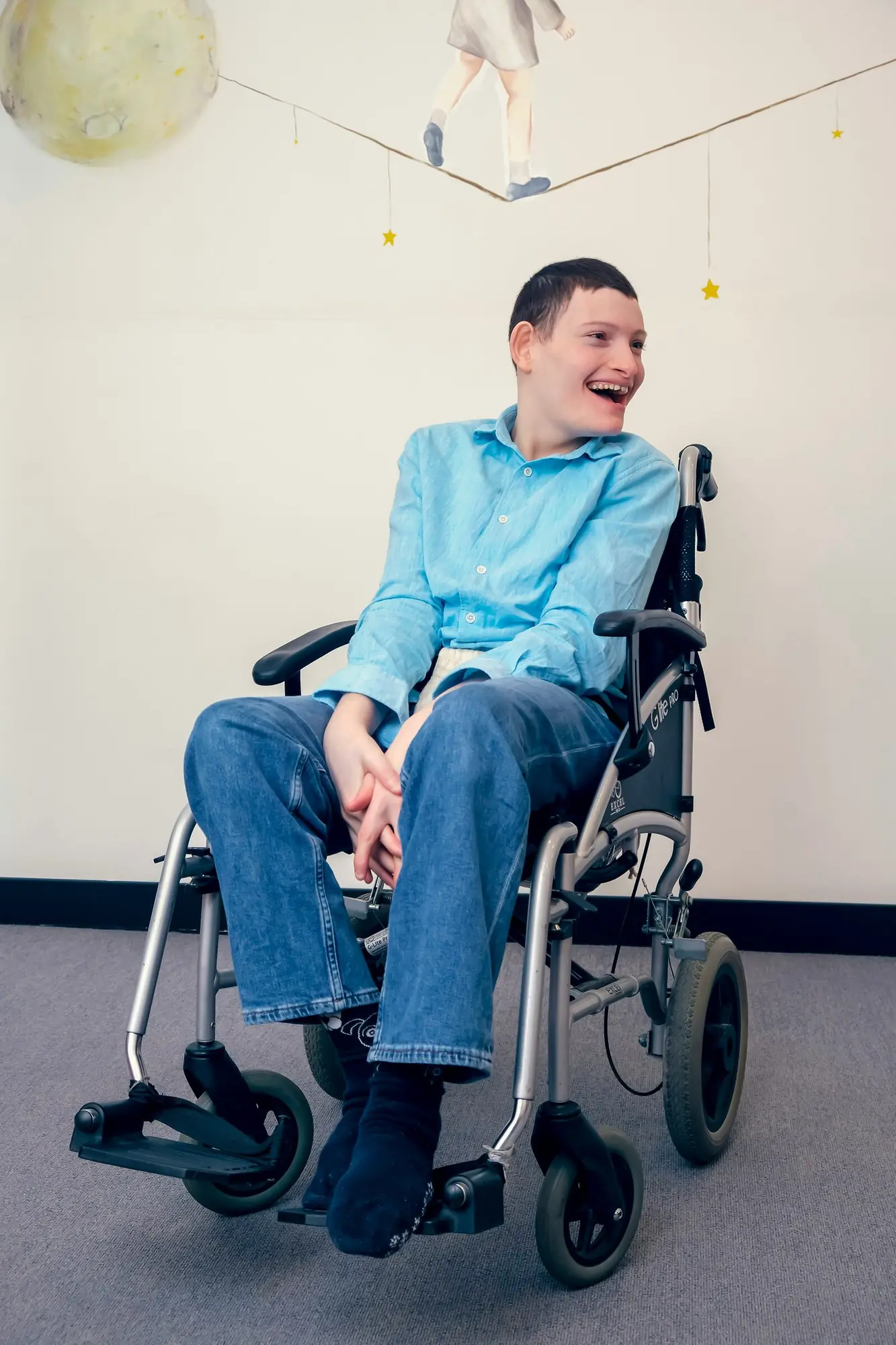 A young man in a wheelchair laughs in a brightly decorated room